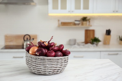 Basket with fresh onions on white marble table in modern kitchen. Space for text