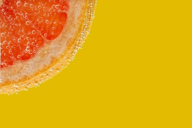 Slice of grapefruit in sparkling water on yellow background, closeup with space for text. Citrus soda