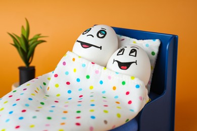 Photo of Eggs with drawn happy faces in small bed on orange background