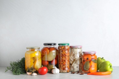 Fresh vegetables and jars of pickled products on light grey table