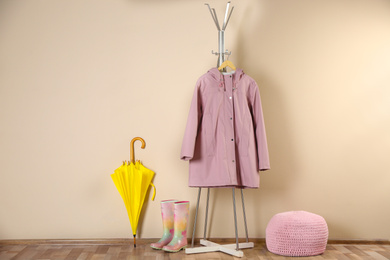 Yellow umbrella, raincoat and rubber boots near beige wall