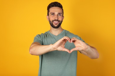 Happy man making heart with hands on yellow background