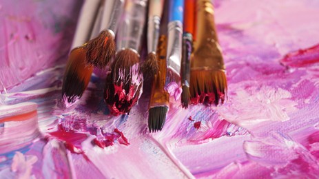 Photo of Brushes on canvas with mixed bright paints, closeup