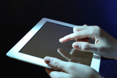 Woman using tablet on dark background, closeup