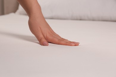 Woman touching soft white bedsheet, closeup view