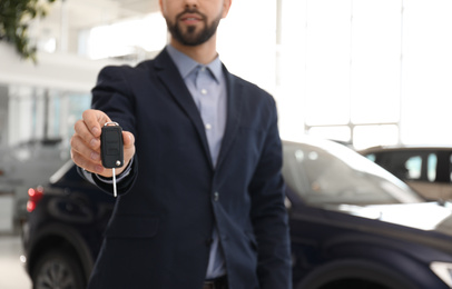Salesman with key in modern car salon, closeup