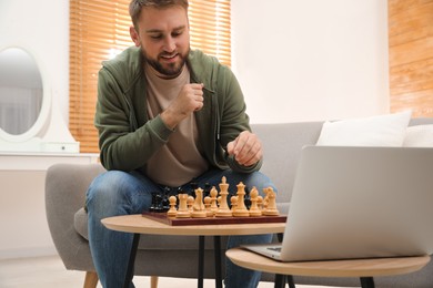 Young man playing chess with partner through online video chat in living room