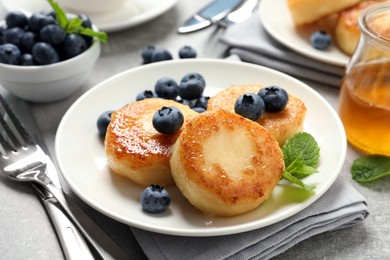 Delicious cottage cheese pancakes with blueberries, mint and honey on light grey table, closeup