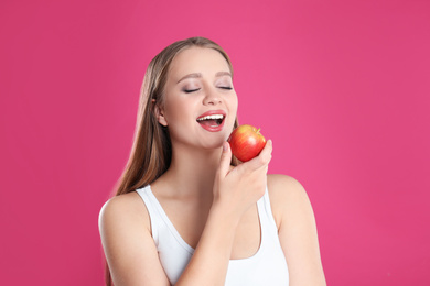 Photo of Young woman with apple on pink background. Vitamin rich food