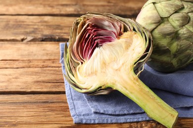 Cut and whole fresh raw artichokes on wooden table, closeup. Space for text