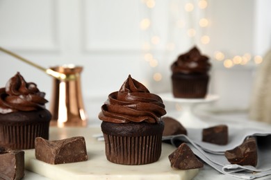 Delicious chocolate cupcake with cream on table against blurred lights. Space for text