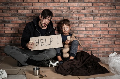 Poor man with his son asking for help near brick wall