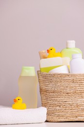 Photo of Wicker basket with baby cosmetic products, bath accessories and rubber ducks on white table against grey background