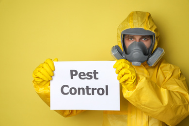 Man wearing protective suit with insecticide sprayer holding sign PEST CONTROL on yellow background
