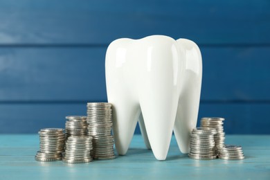 Ceramic model of tooth and coins on light blue wooden table. Expensive treatment