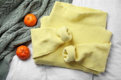 Beautiful yellow warm sweater, plaid and tangerines on white bedsheet,  flat lay