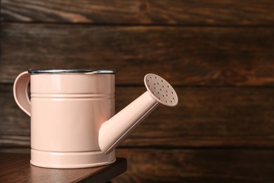 Photo of Pink metal watering can on table against wooden background