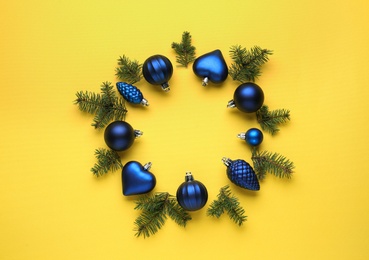Beautiful festive wreath made of blue Christmas balls and fir tree branches on yellow background, top view