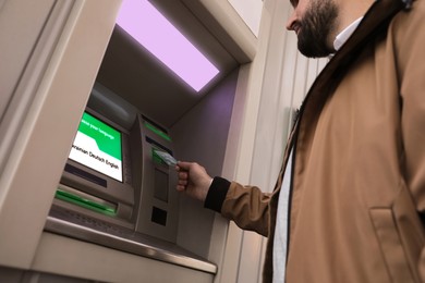 Man inserting credit card into cash machine outdoors, low angle view