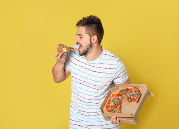 Handsome man eating tasty pizza on yellow background