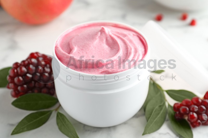 Photo of Fresh pomegranate and jar of facial mask on white marble table, closeup. Natural organic cosmetics