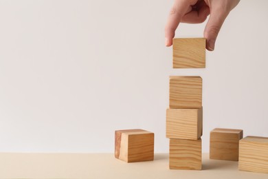 Woman stacking wooden cubes at table, closeup and space for text. Management concept