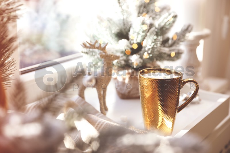 Golden cup of cocoa and Christmas decor on window sill indoors