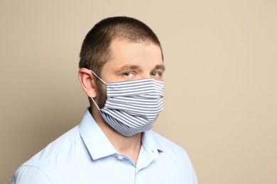 Man wearing handmade cloth mask on beige background. Personal protective equipment during COVID-19 pandemic