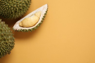 Fresh ripe durians on orange background, flat lay. Space for text