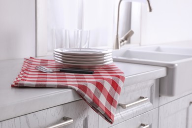 Dry towel and clean dishware on white countertop near sink in kitchen