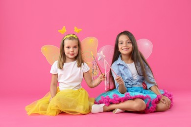 Cute little girls in fairy costumes with wings and magic wands on pink background