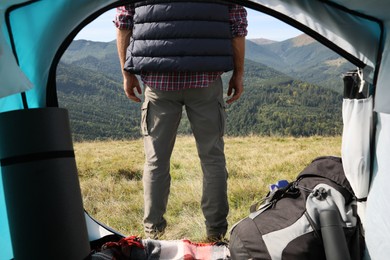 Man in mountains on sunny day, view from camping tent