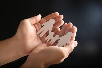 Man holding paper silhouette of family in hands on dark background, closeup