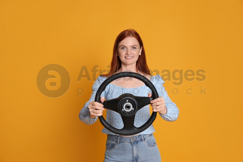 Happy young woman with steering wheel on yellow background