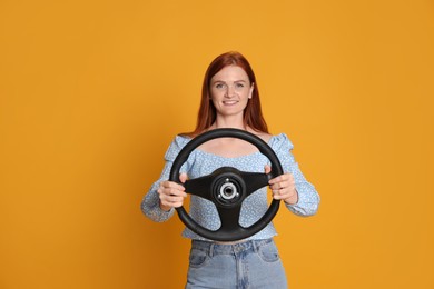 Happy young woman with steering wheel on yellow background