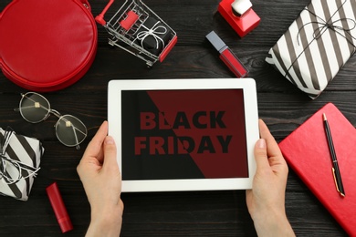 Woman with tablet surrounded by gifts and accessories at wooden table, top view. Black Friday sale