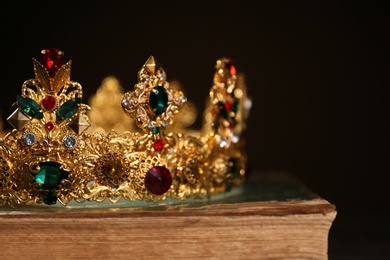 Beautiful golden crown on old book against black background, closeup. Fantasy item