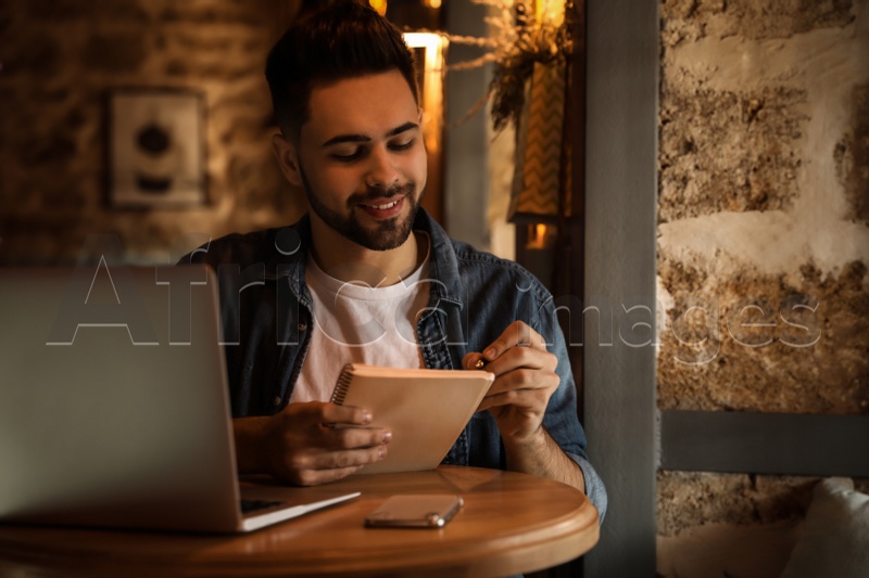 Young blogger writing in notebook at table indoors
