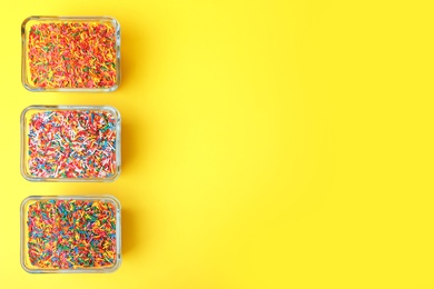 Colorful sprinkles in bowls on yellow background, flat lay with space for text. Confectionery decor