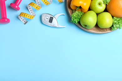 Fruits, dumbbells, measuring tape and digital caliper on light blue background, flat lay with space for text. Visiting nutritionist