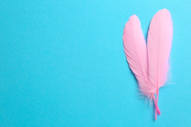 Beautiful pink feathers on light blue background, top view. Space for text