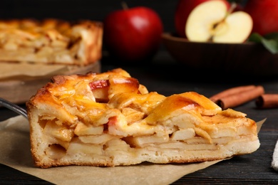 Slice of traditional apple pie on black wooden table, closeup