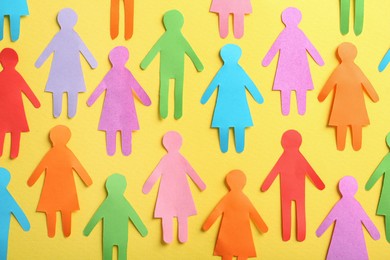 Photo of Many different paper human figures on yellow background, flat lay. Diversity and inclusion concept