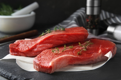 Fresh raw beef cut with thyme on black table, closeup