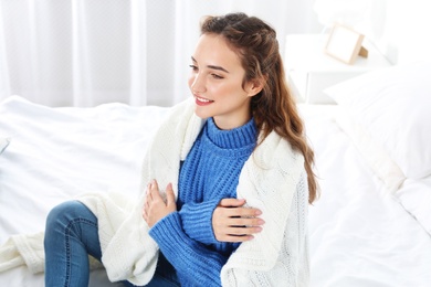Beautiful teenage girl in warm cozy sweater with plaid sitting on bed at home