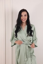 Pretty young woman in beautiful light silk robe near white wall