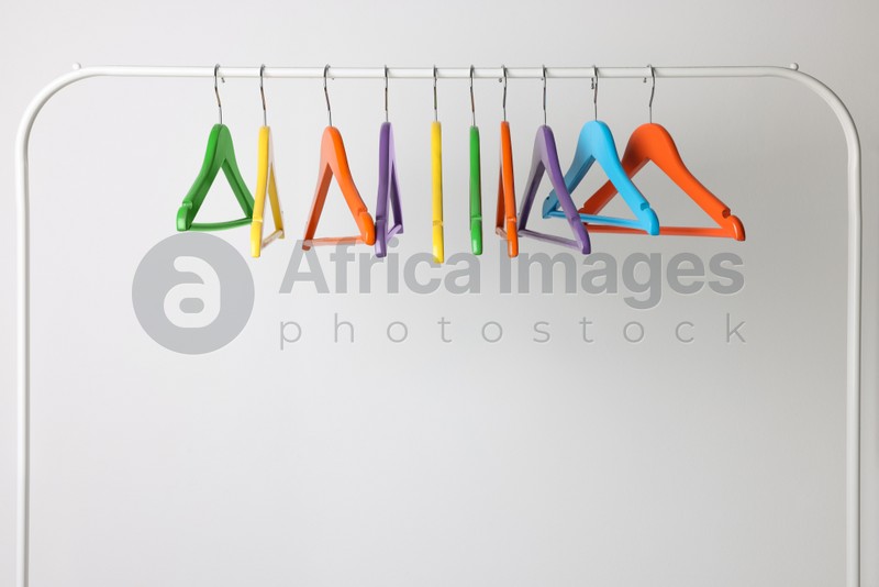 Bright clothes hangers on metal rack against light background