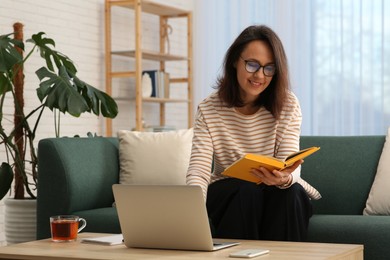 Woman with modern laptop and book learning in living room