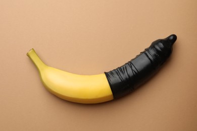 Banana with condom on pale orange background, top view. Safe sex concept