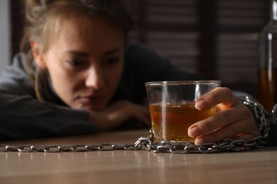 Alcohol addiction. Woman chained with glass of liquor at wooden table in room, focus on hand
